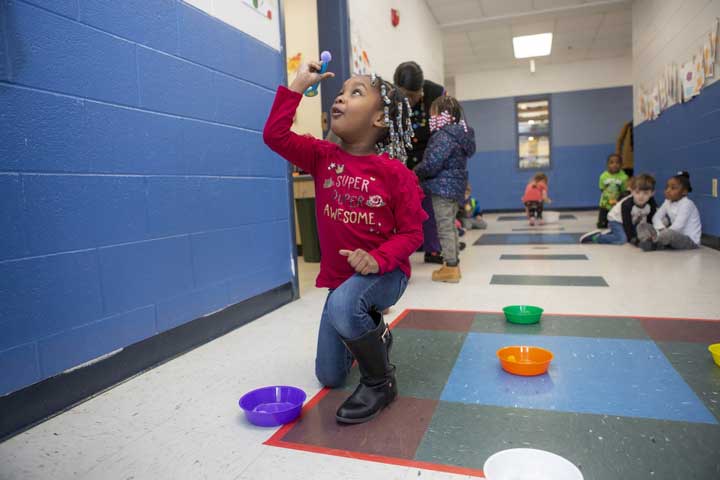 A young girl in the hallway trying to balance a ball.