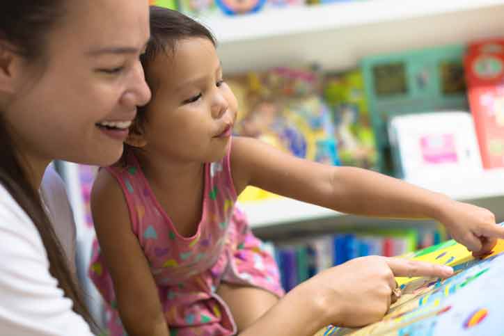 Parent and child pointing at a letter in book.